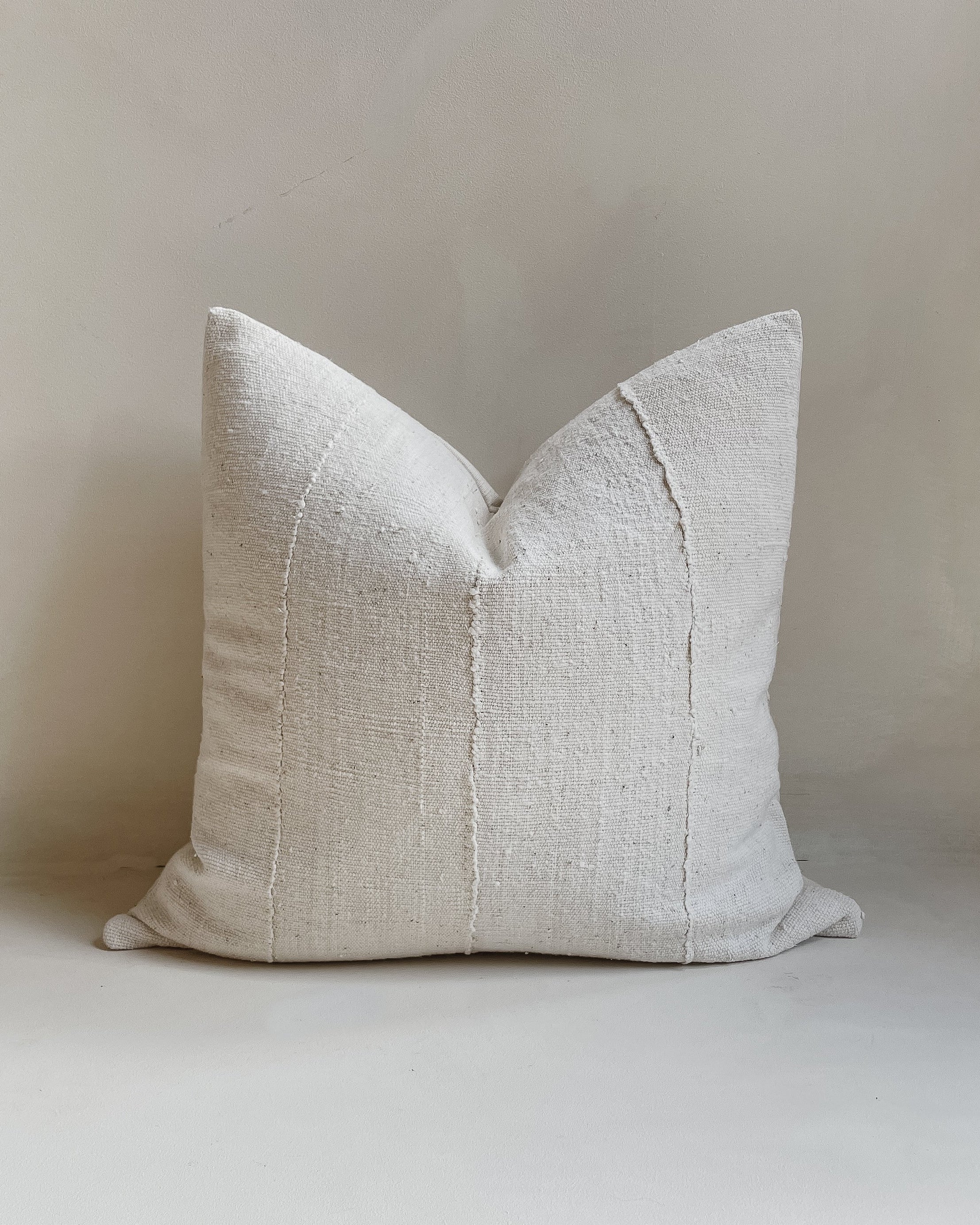 Front view of a 20x20” square cushion cover made from authentic ‘Bogolan’ mudcloth material native to Mali, Western Africa. The cotton is raw and rustic with an organic white textured finish. It has a textured cotton back and an invisible zipper. Made in the United Kingdom. Displayed against a neutral limewash background