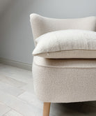Side view of a 20x20” square cushion cover made from authentic ‘Bogolan’ mudcloth material native to Mali, Western Africa. The cotton is raw and rustic with an organic white textured finish. It has a textured cotton back and an invisible zipper. Made in the United Kingdom. Displayed on a neutral cream boucle chair