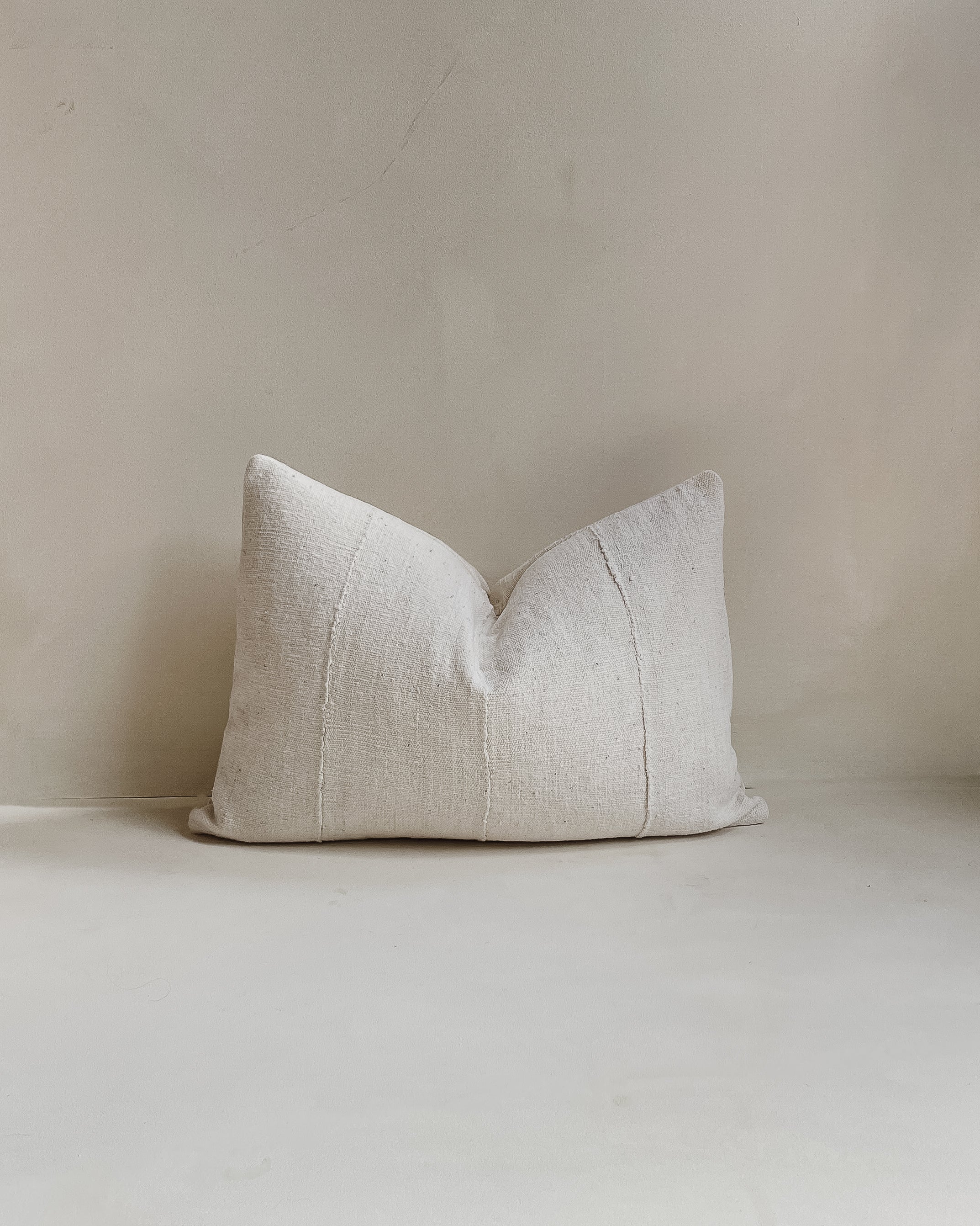 Front view of a 14x20” rectangle lumber cushion cover made from authentic ‘Bogolan’ mudcloth material native to Mali, Western Africa. The cotton is raw and rustic with an organic white textured finish. It has a textured cotton back and an invisible zipper. Made in the United Kingdom. Displayed against a neutral limewash background