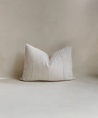 Front view of a 14x20” rectangle lumber cushion cover made from authentic ‘Bogolan’ mudcloth material native to Mali, Western Africa. The cotton is raw and rustic with an organic white textured finish. It has a textured cotton back and an invisible zipper. Made in the United Kingdom. Displayed against a neutral limewash background