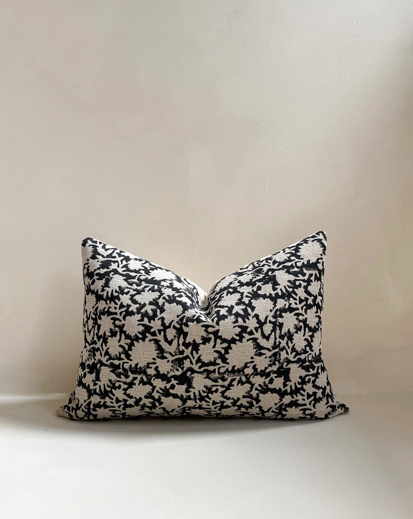 Front view of a 14x20” rectangle lumber luxury heavy linen hand-blocked cushion cover featuring a delicate organic black floral pattern. It has a soft cotton back and an invisible zipper. Hand-block material is produced in Jaipur, India. Cushion cover is made in the UK. Displayed against a neutral limewash background